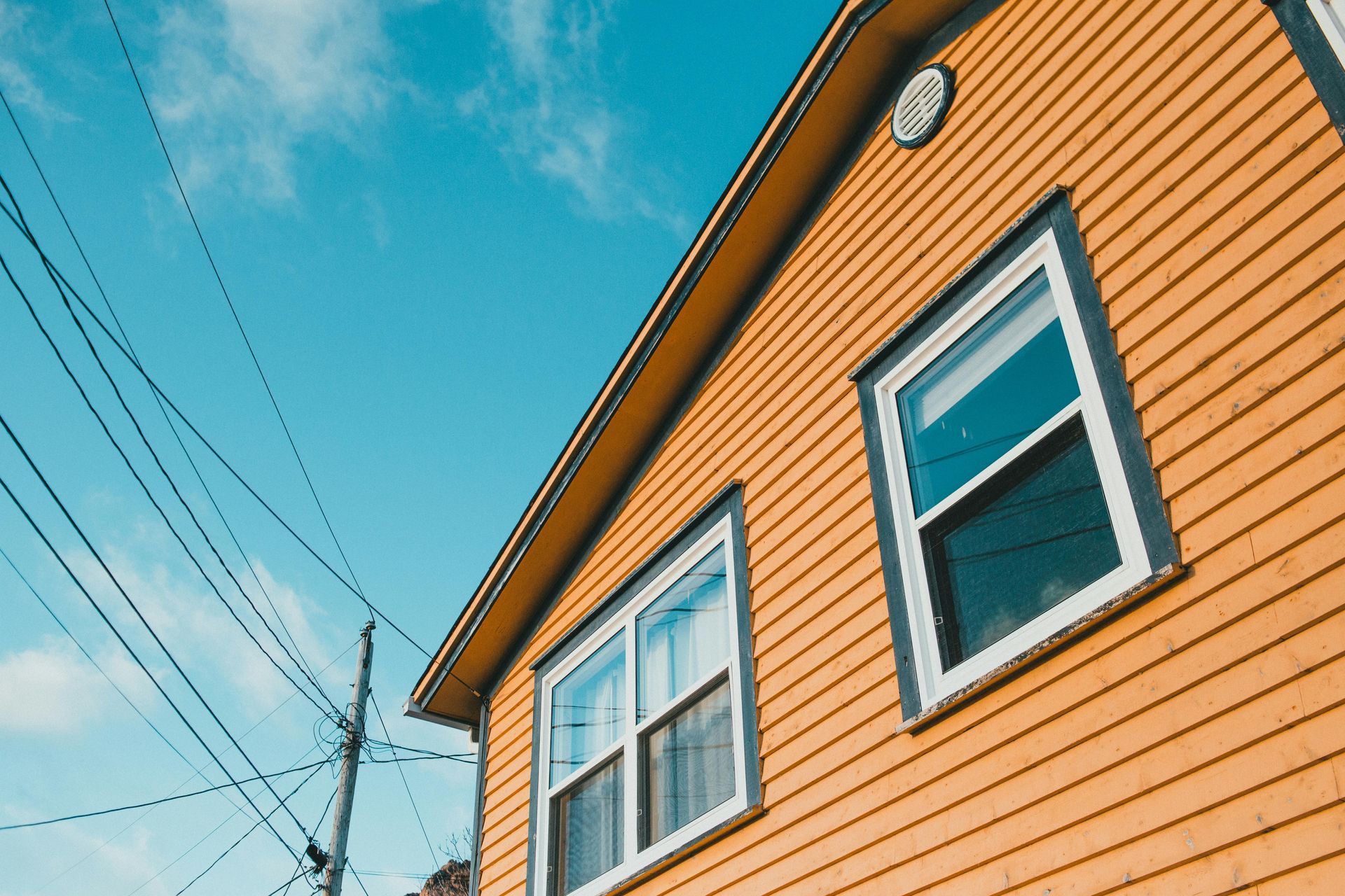 Orange house siding with white-trimmed windows against a blue sky and power lines