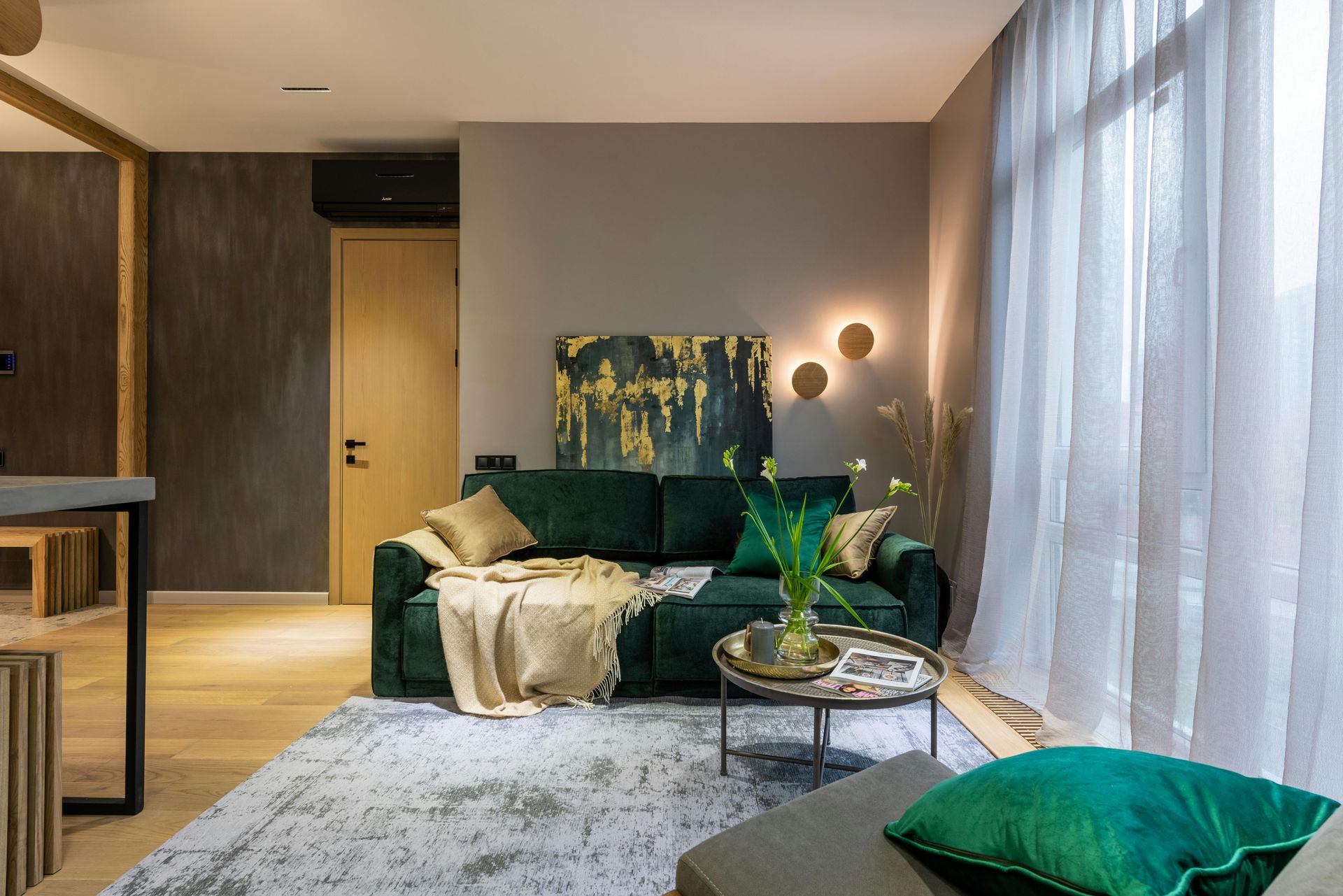Modern living room with green sofa, large windows, soft lighting, and a patterned rug