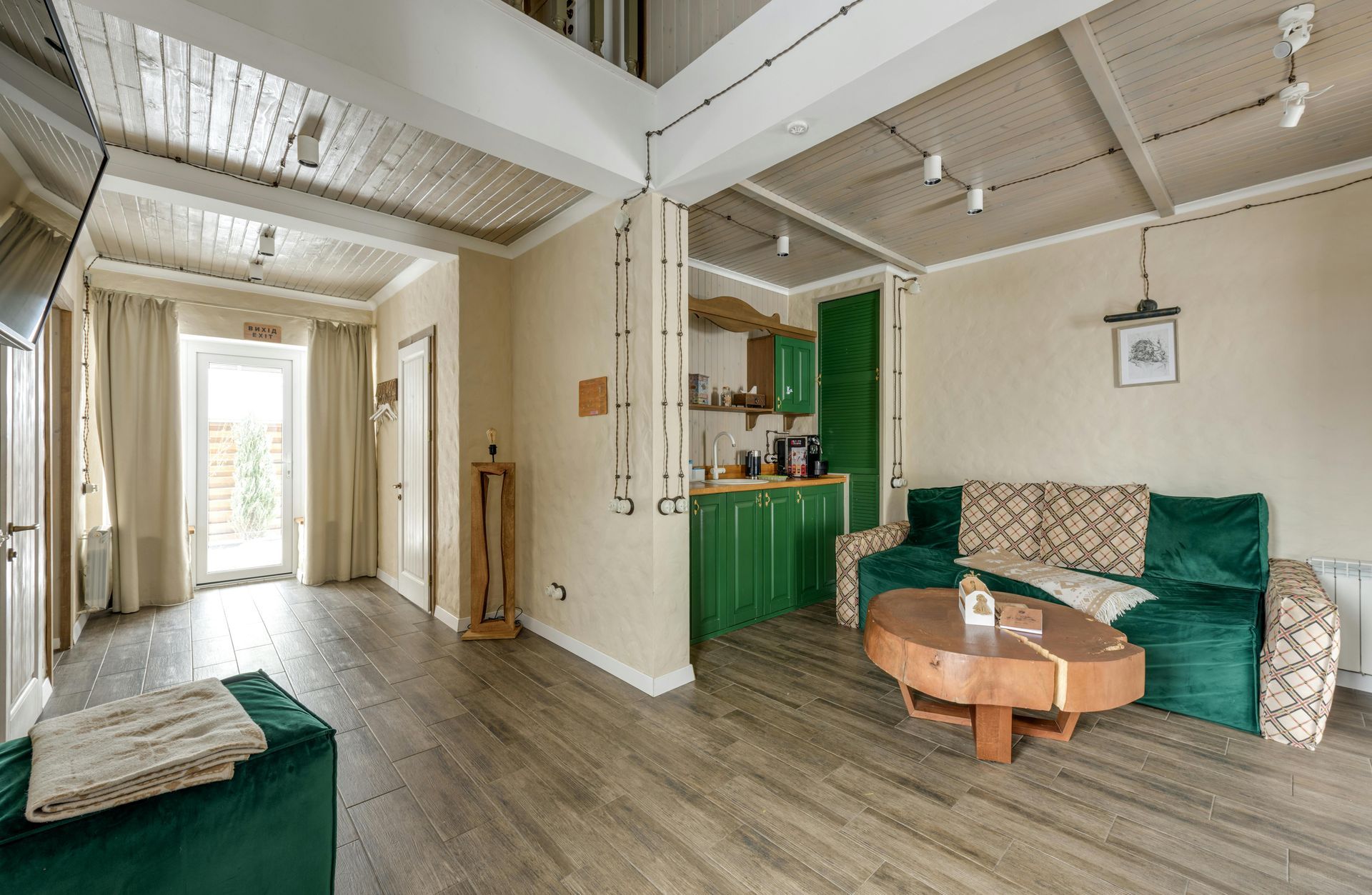 Bright living room with green sofa, round wooden coffee table, and kitchenette in the background.