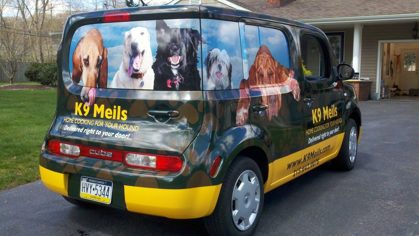 K9 Meals delivery van with dog graphics and yellow accents parked in a driveway