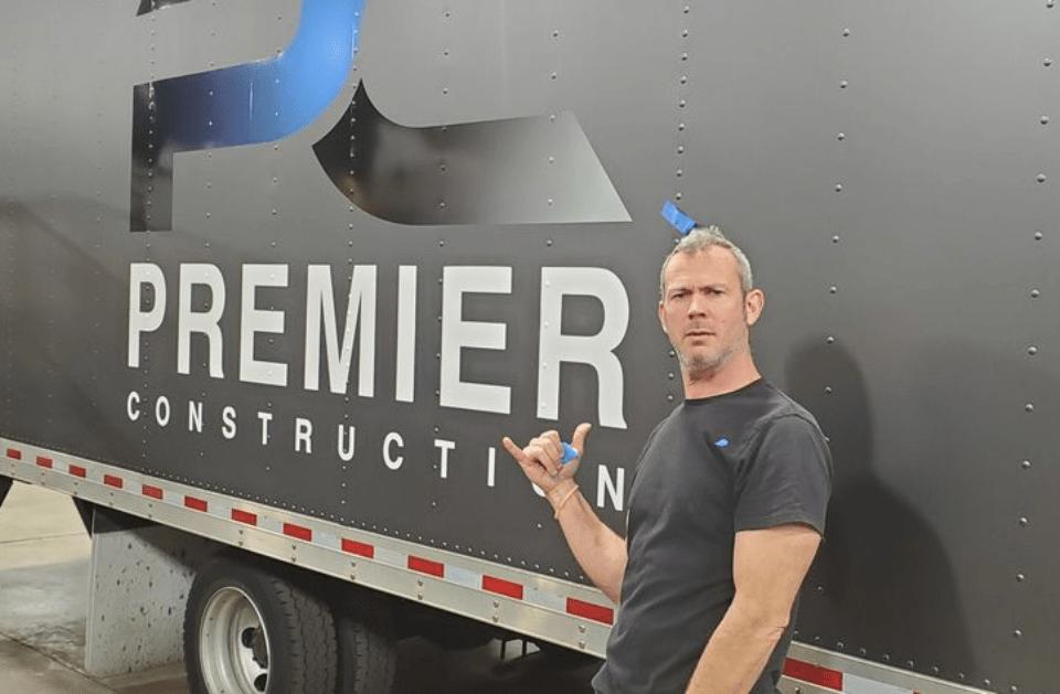 Man standing beside a Premier Construction trailer, pointing at the logo.