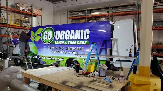 Blue van wrapped for GO ORGANIC in a workshop, with tools and ladders around it.