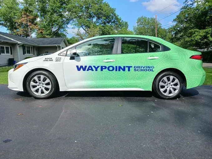 Waypoint-branded white-and-green sedan parked in a driveway on a sunny suburban street