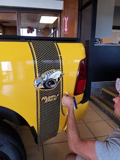 Hand applying a car decal to a yellow vehicle’s rear hatch