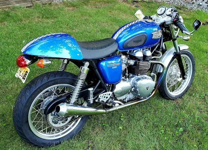 Blue classic motorcycle parked on grass, side view with chrome details and black seat
