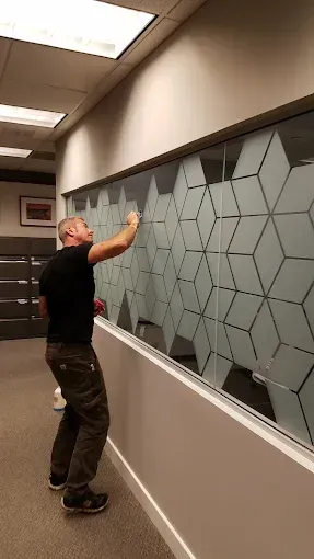 Person placing hexagonal tiles on a large wall display in an office hallway