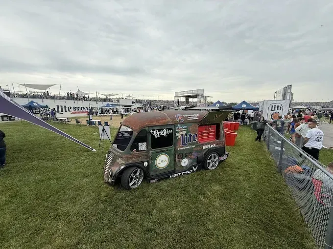 Custom coffee truck at an outdoor event with a crowd and tents under a cloudy sky