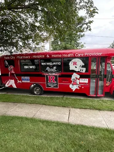 Red mobile healthcare van parked by a sidewalk and trees, covered with Rutgers and RWJ Barnabas Health branding