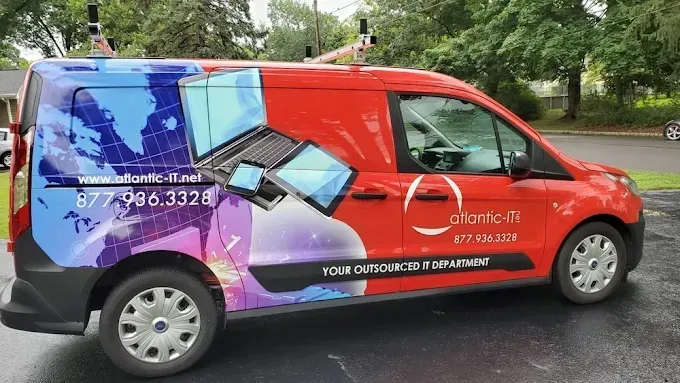 Red promotional van with laptop graphics parked on a tree-lined street