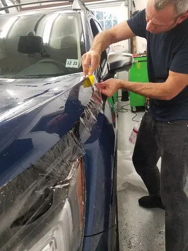 Technician applying protective film to a dark blue car in a garage