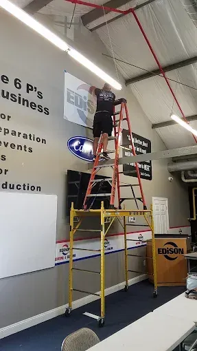 Person on a ladder installing signs in a showroom with white walls and a black floor.