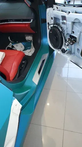 A car interior with a red seat and exposed white door panel in a teal vehicle shell.