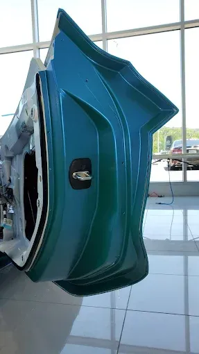 Teal industrial machine component with a pointed front, displayed indoors on a glossy floor.