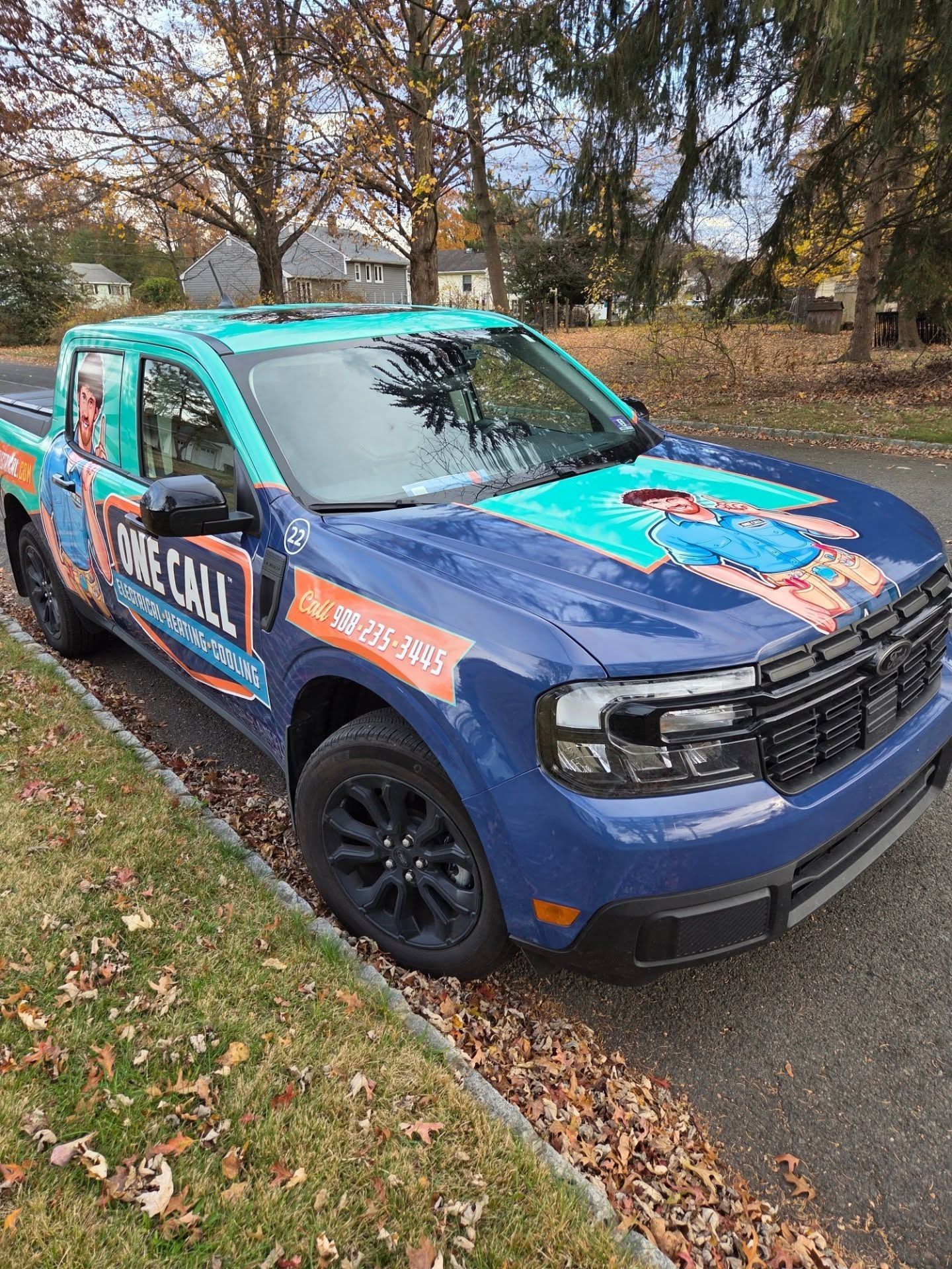 Blue and teal roadside assistance truck parked on a leaf-covered street in autumn