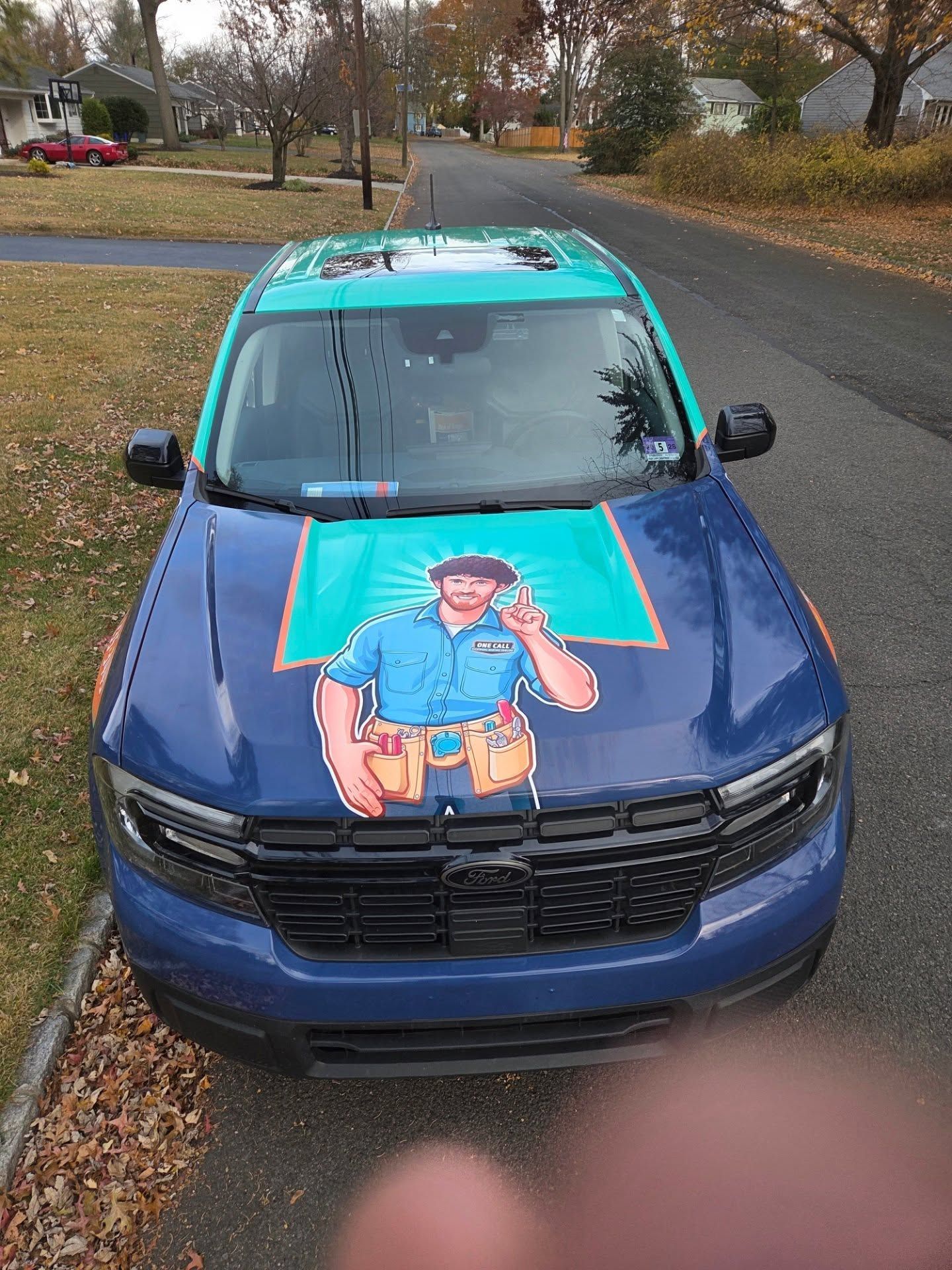 Blue car parked on a wet street, with a colorful cartoon decal on the hood and teal roof.