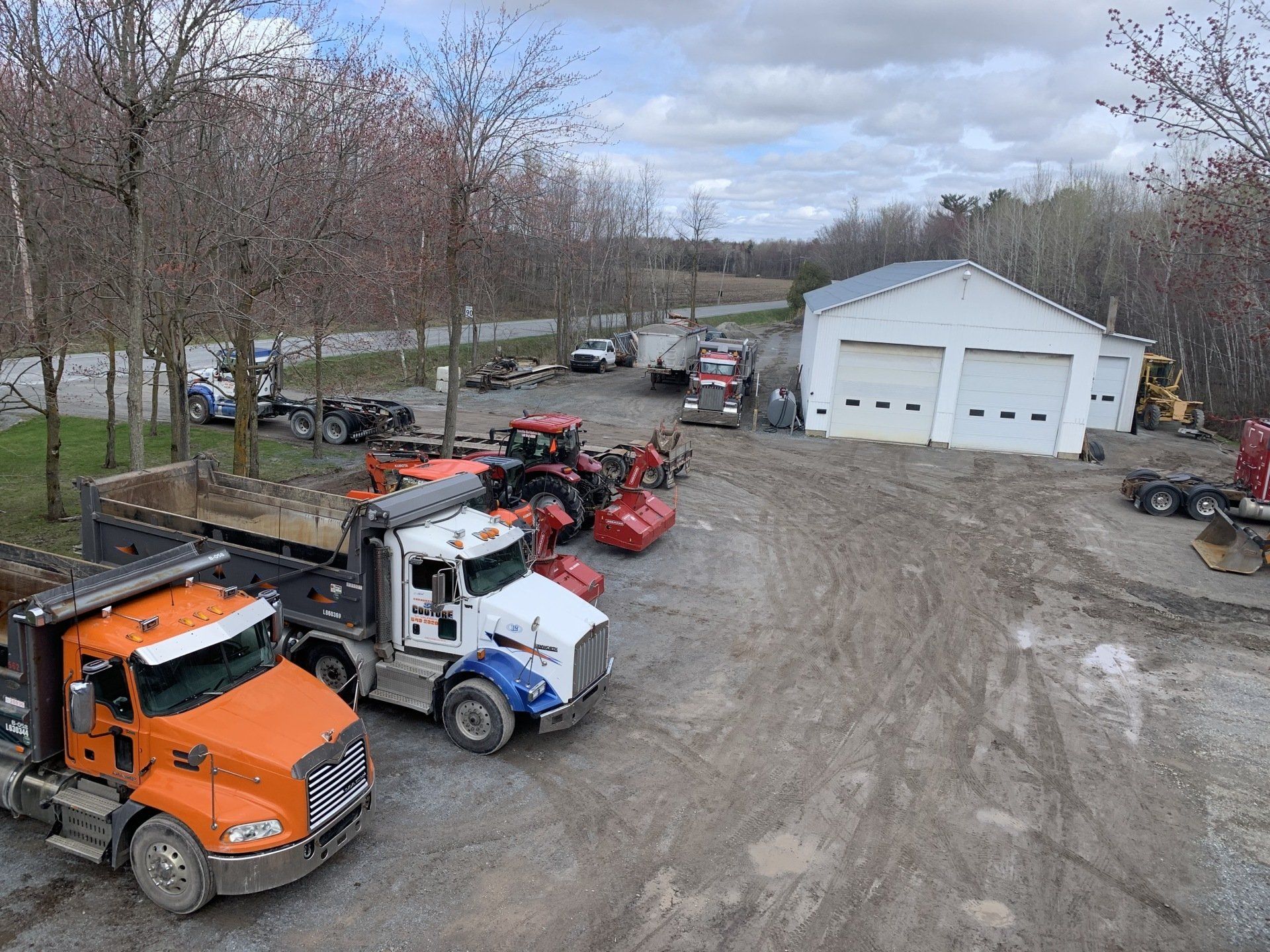 Une rangée de camions est garée dans un terrain sale devant un garage.