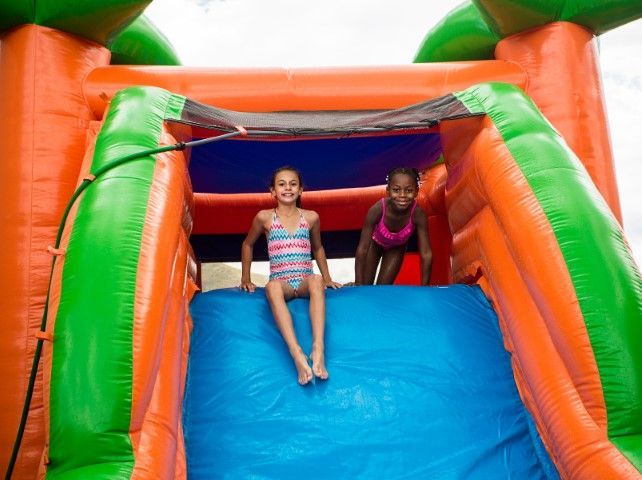 Two children sit at the top of a colorful inflatable slide, smiling.