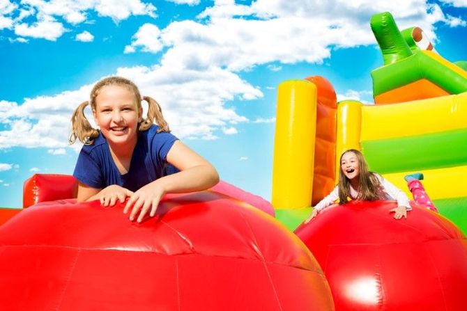 Children smiling on a colorful inflatable bounce house under a bright blue sky