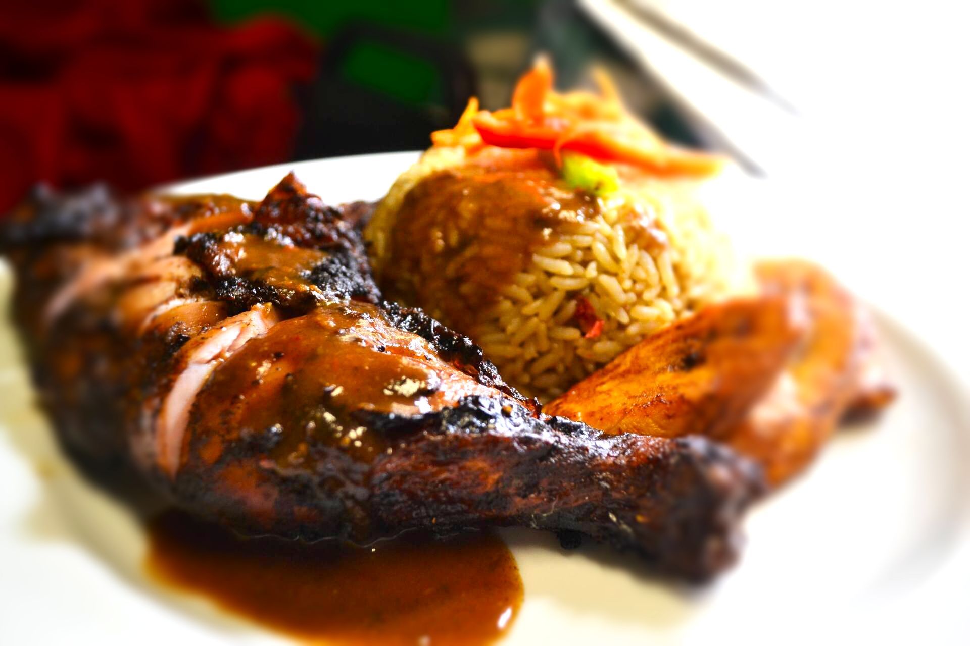 A white plate topped with the best succulent piece of  Seasoned Chicken jerk chicken meat and rice