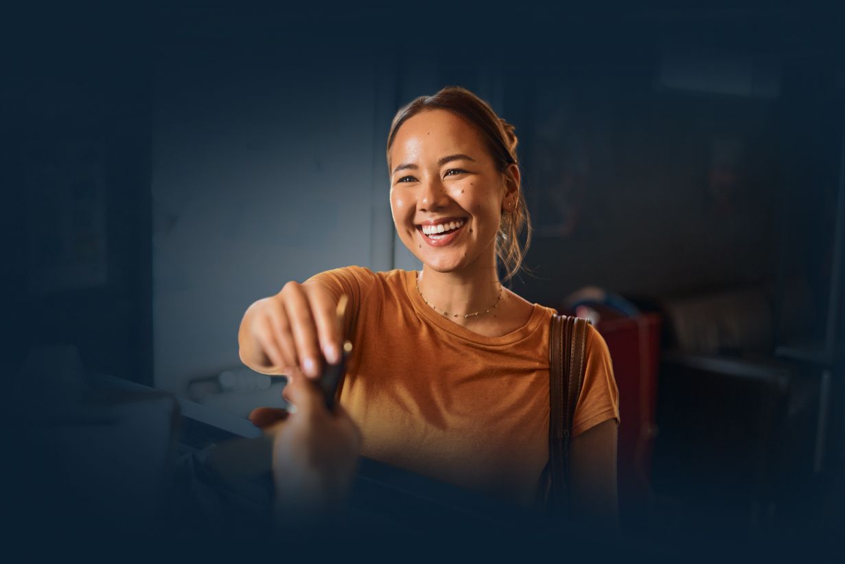 Smiling person in an orange top reaching toward the camera in a dim room | Coastal Automotive Repair