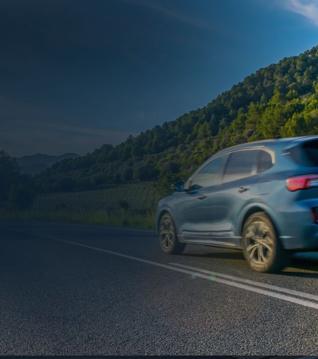 Blue SUV driving on a mountain road beside a forested hillside | Coastal Automotive Repair