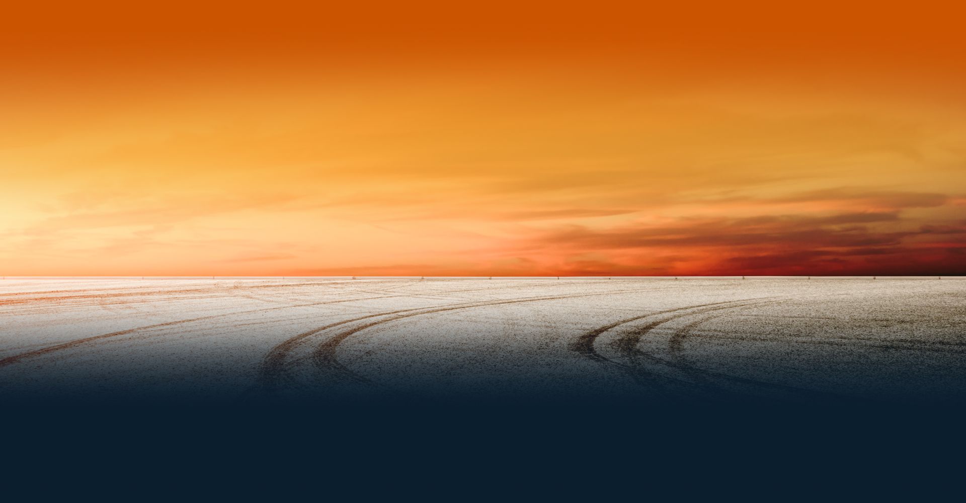 Orange sunset over a snowy flat landscape with tire tracks on the horizon | Coastal Automotive Repair