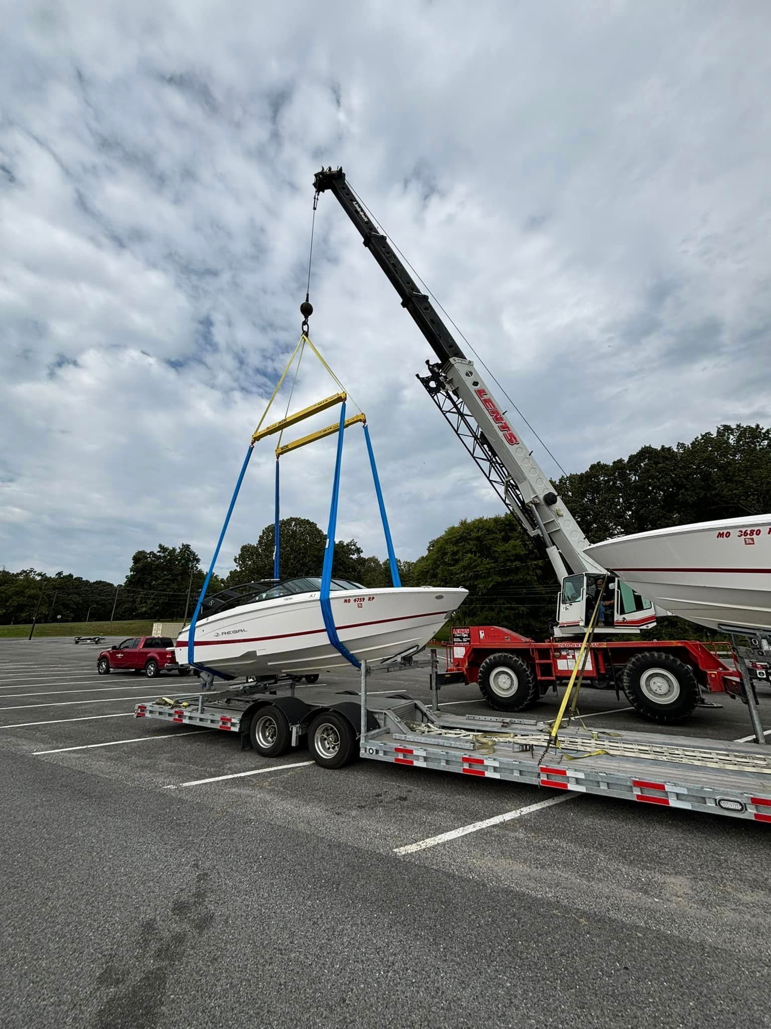 A crane is lifting a boat on a trailer in a parking lot.