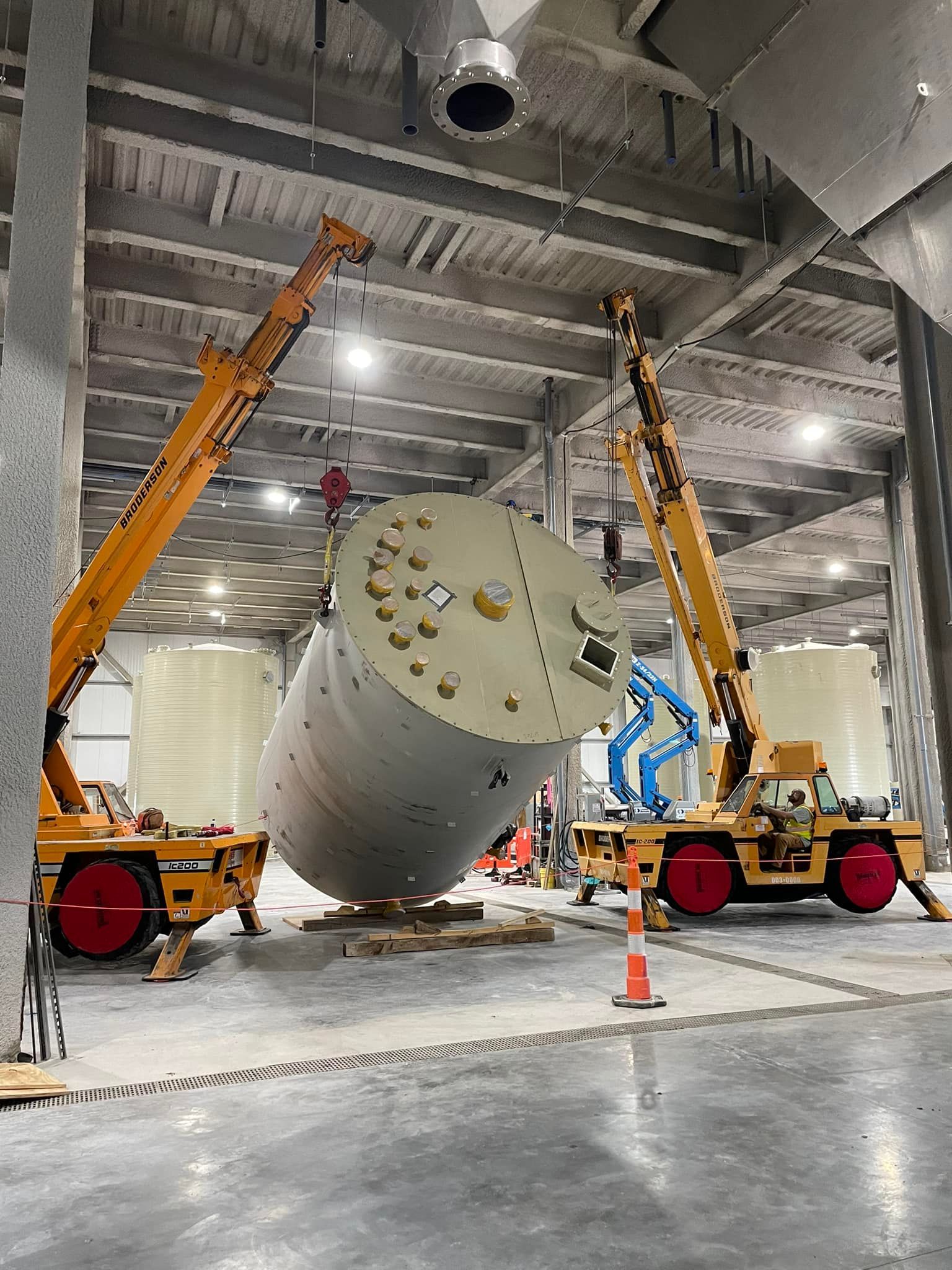 A large tank is being lifted by a crane in a warehouse.