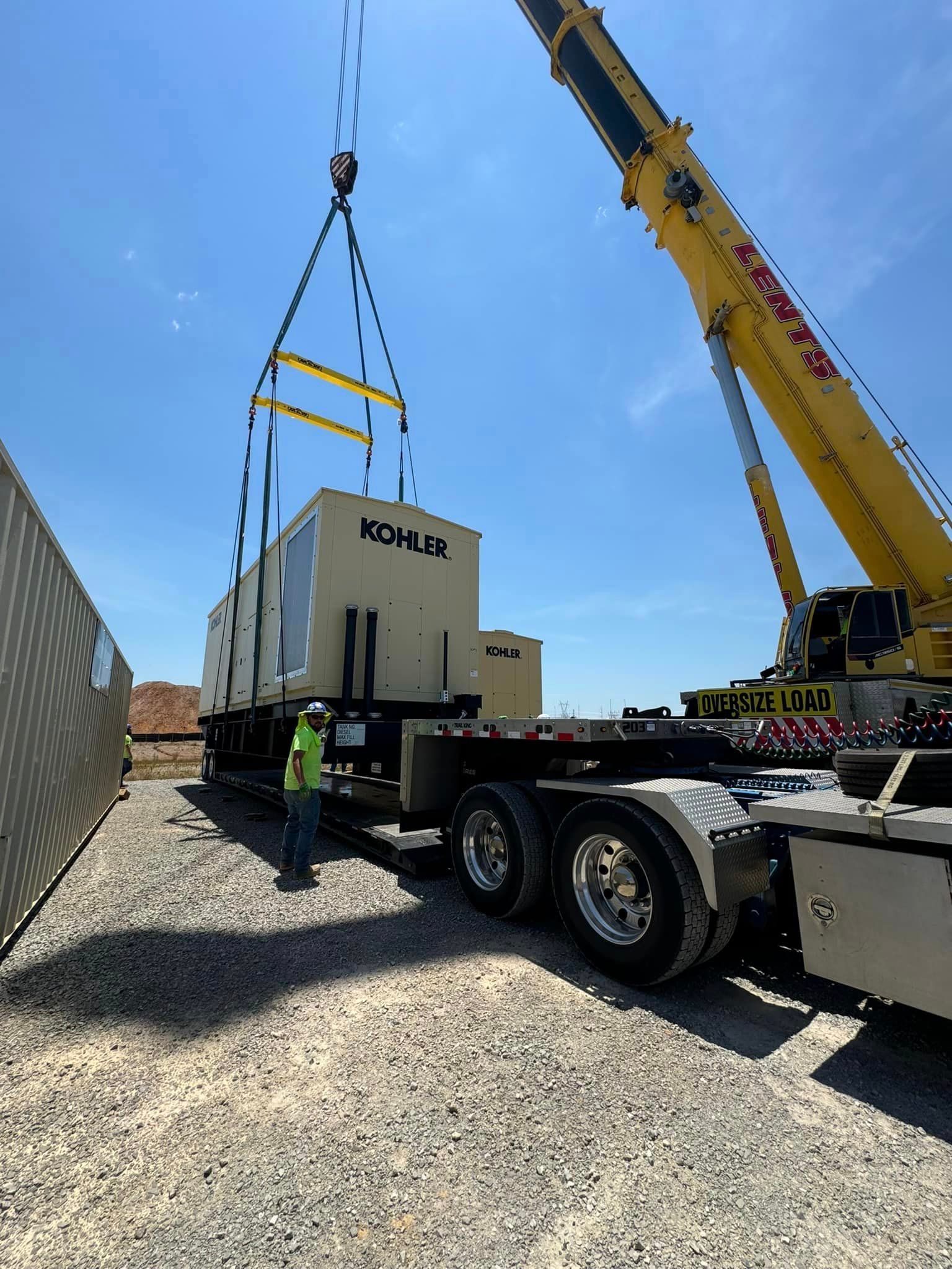 A man is standing next to a crane lifting a box from a truck.