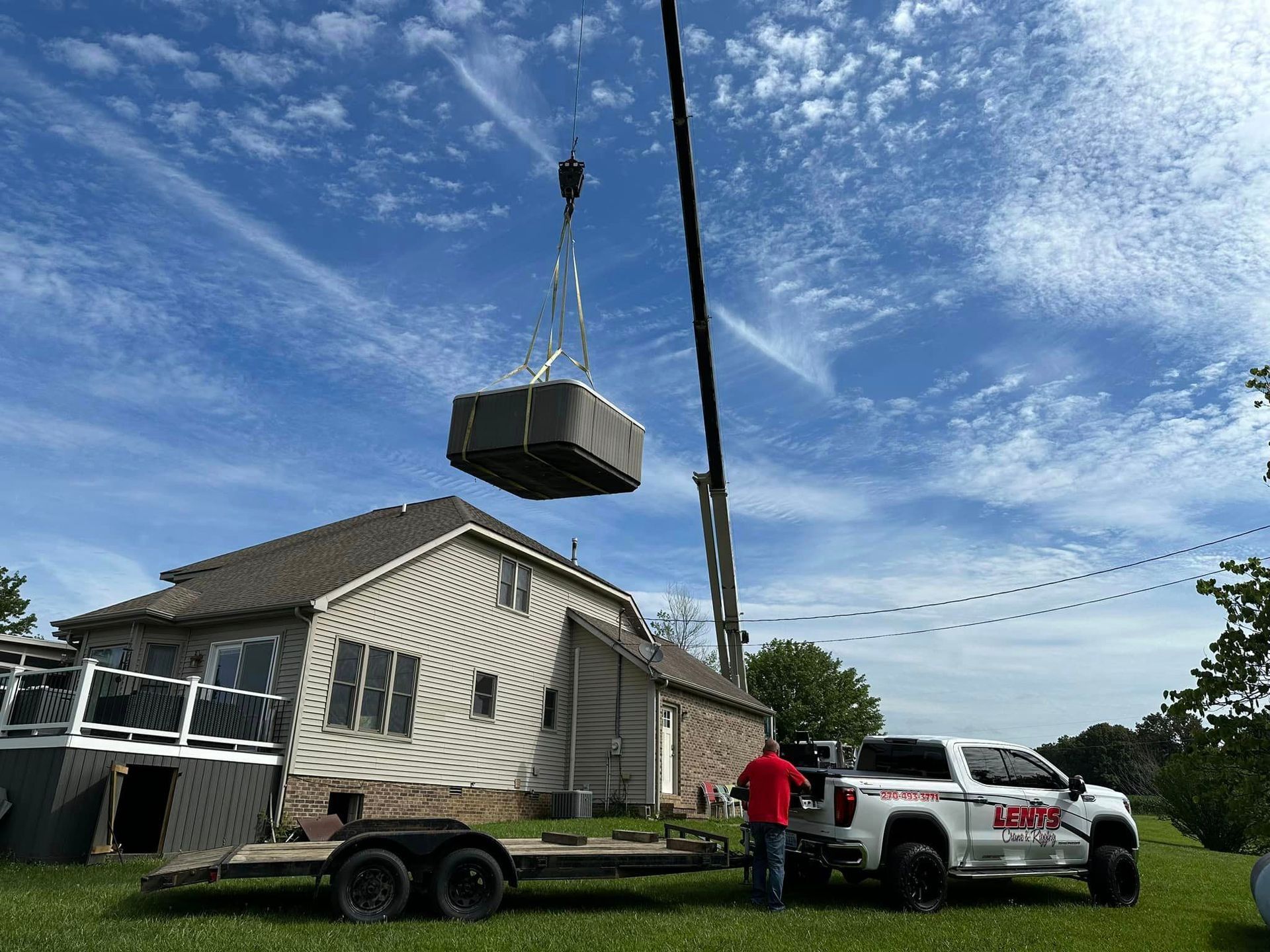 A crane is lifting a pool into a house on a trailer.