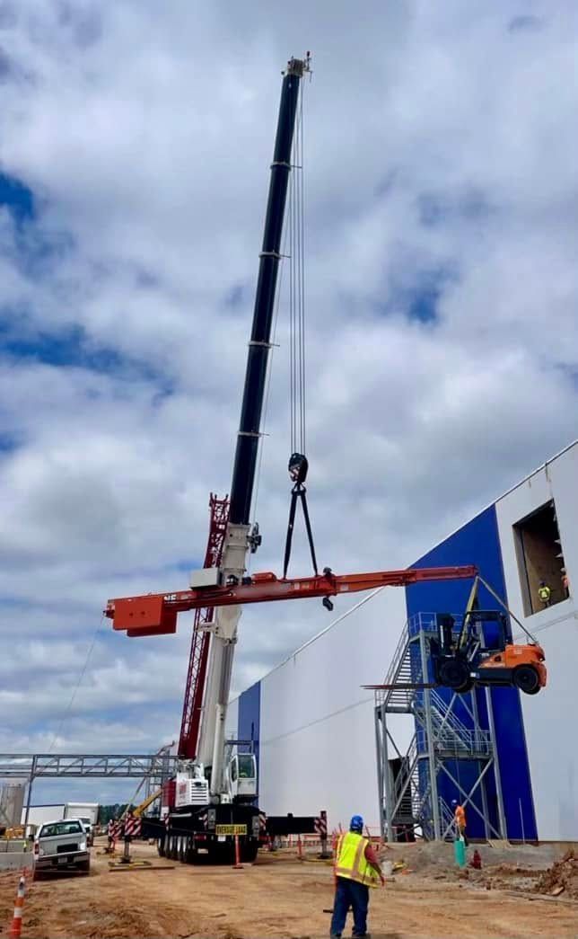A large crane is lifting a large piece of metal in front of a building.