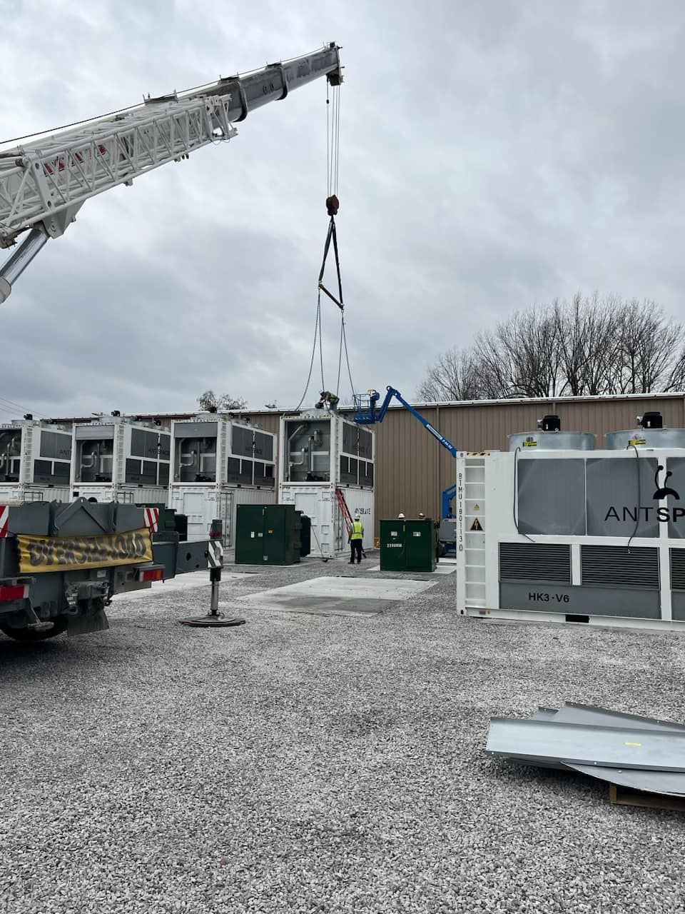 A crane is lifting a piece of metal in front of a building.