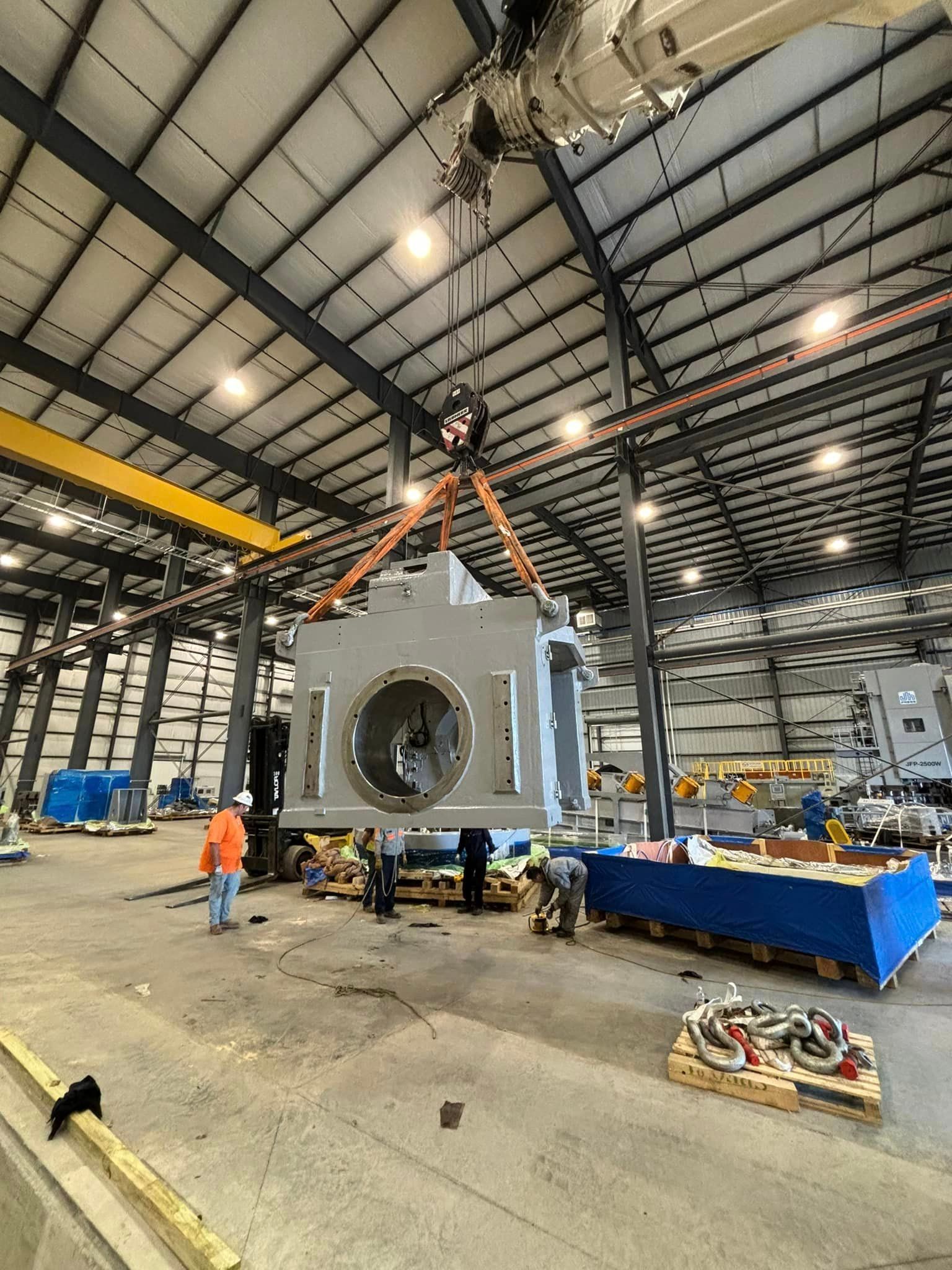 A large piece of metal is being lifted by a crane in a factory.