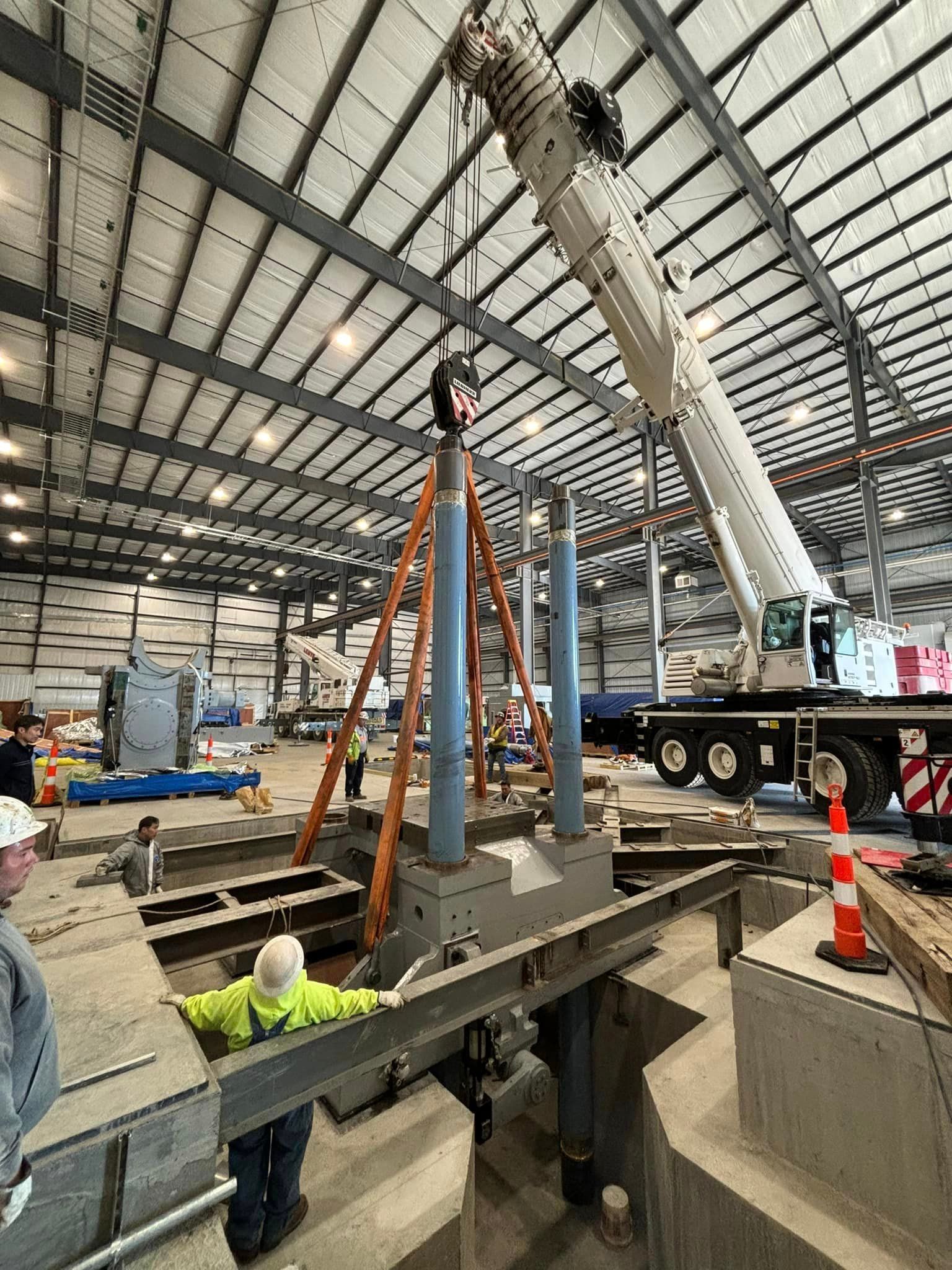 A large crane is being used to lift a large piece of metal in a large warehouse.