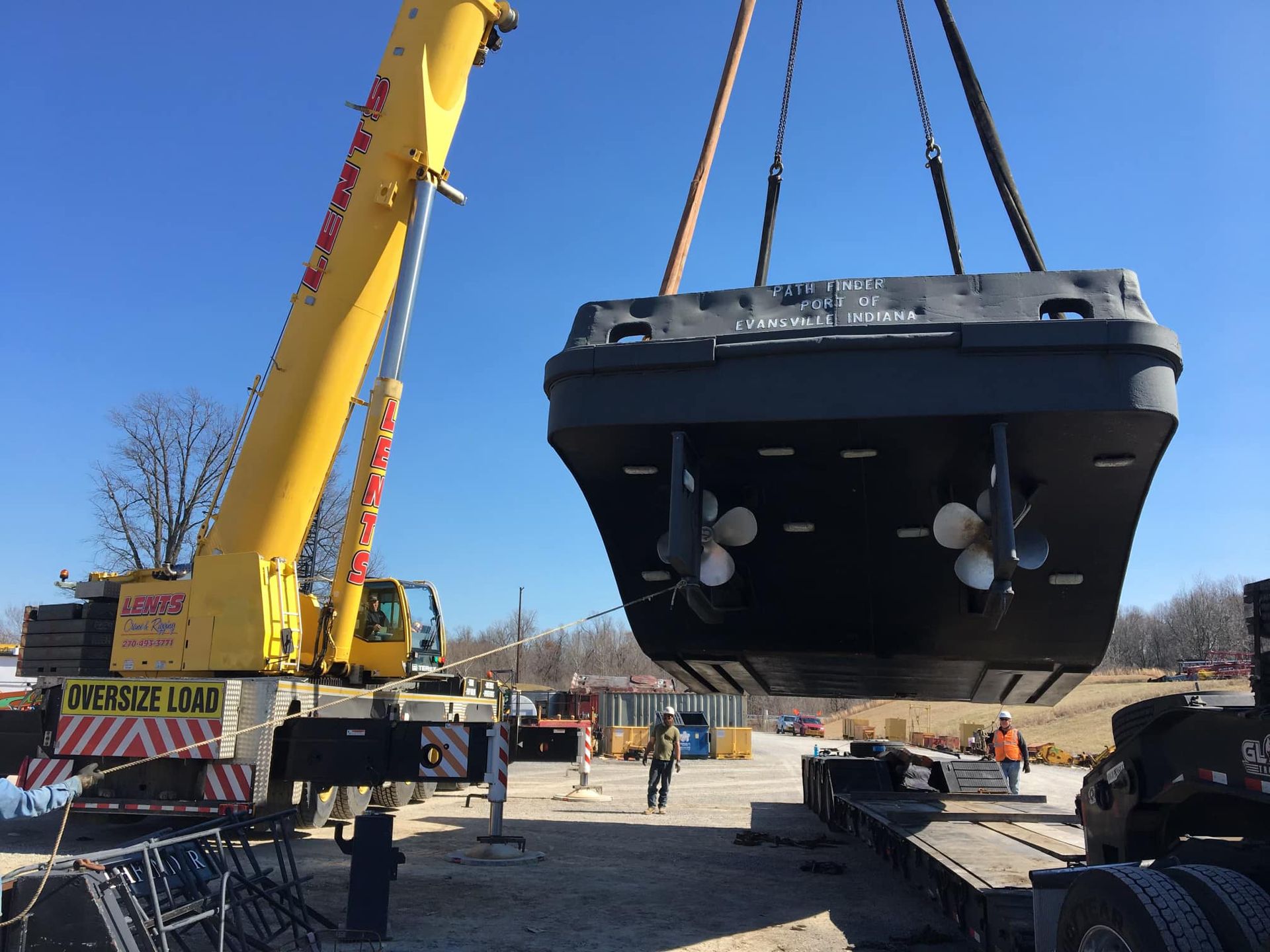 A large yellow crane is lifting a large black object