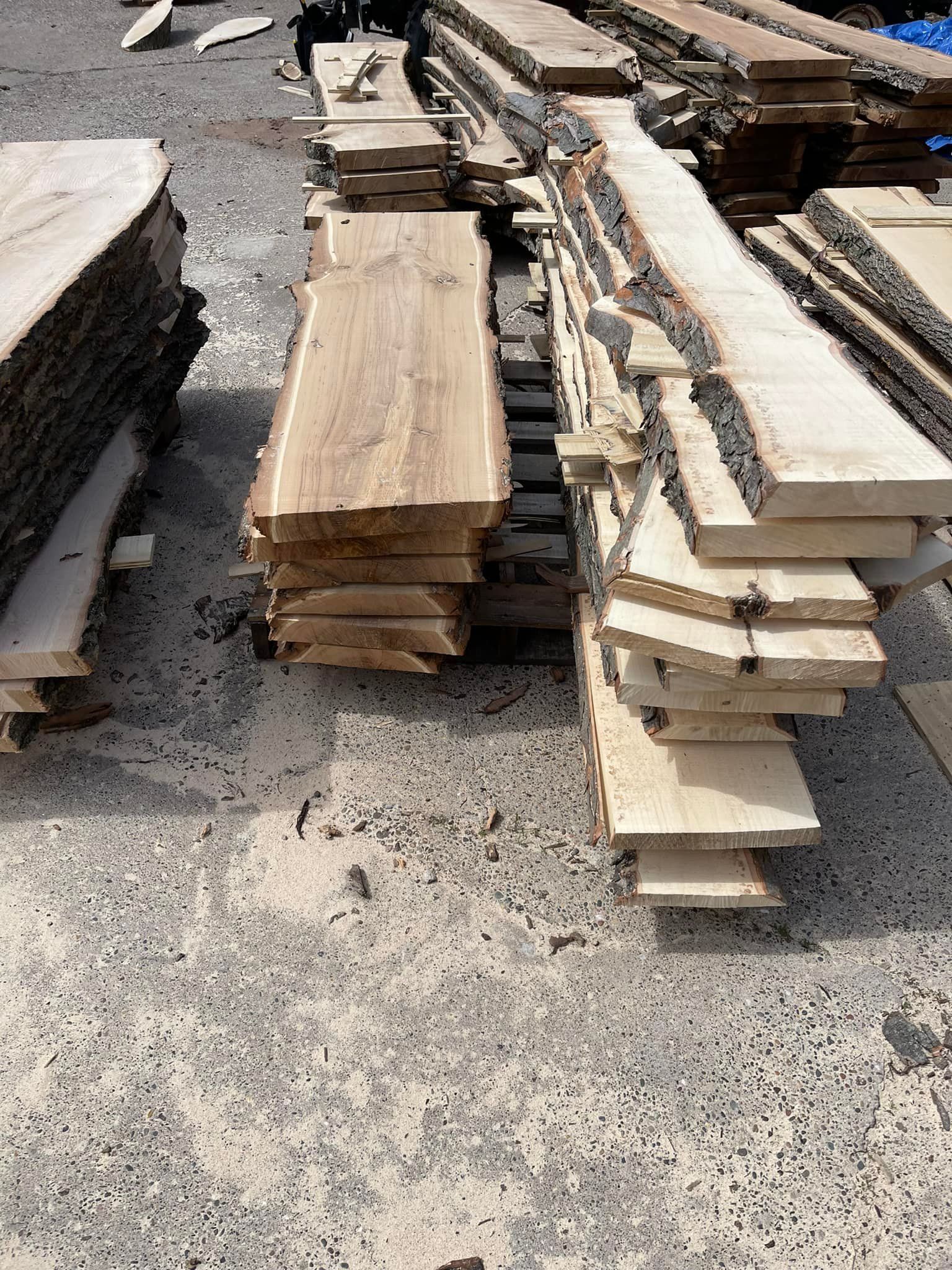 Stacks of rough-cut lumber boards piled on a concrete surface in bright sunlight.