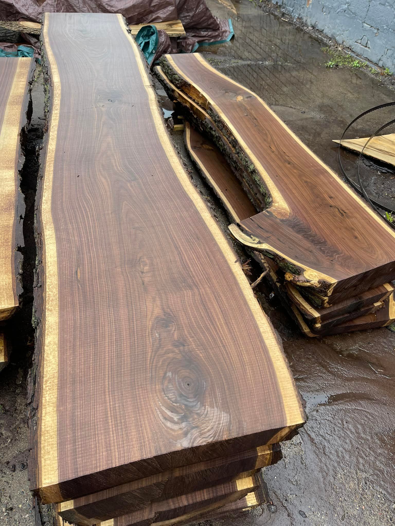 Two long live-edge wooden slabs stacked on pavement, one with a pale resin-filled center channel.