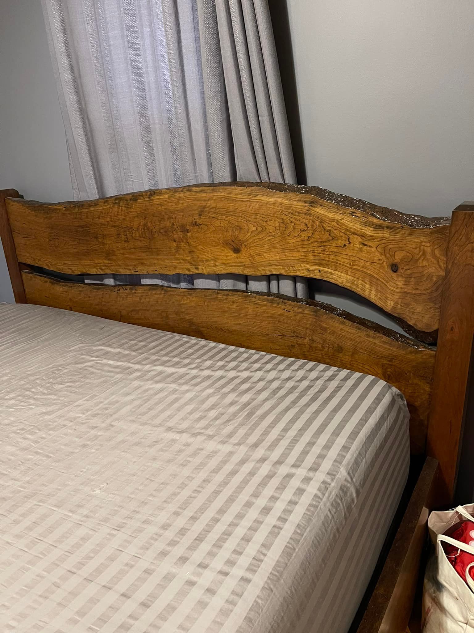 Wooden headboard with a wavy black inlay beside a bed with a beige patterned blanket.