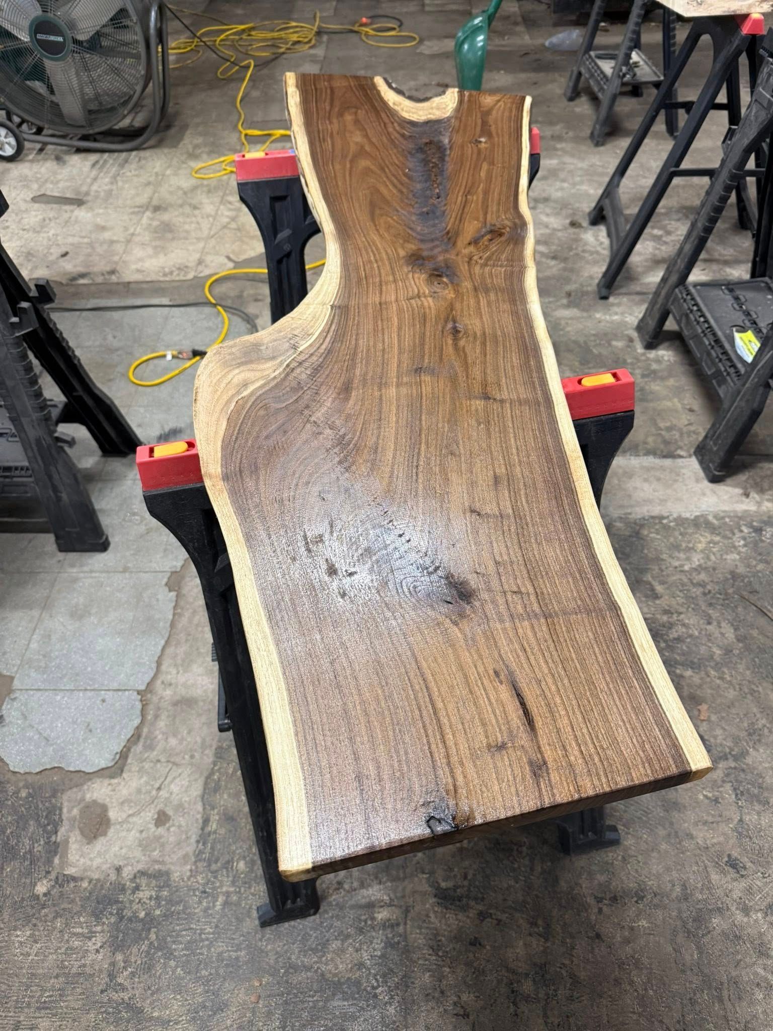 Wood slab on black metal stand in a workshop, with light-colored edges and a glossy finish.