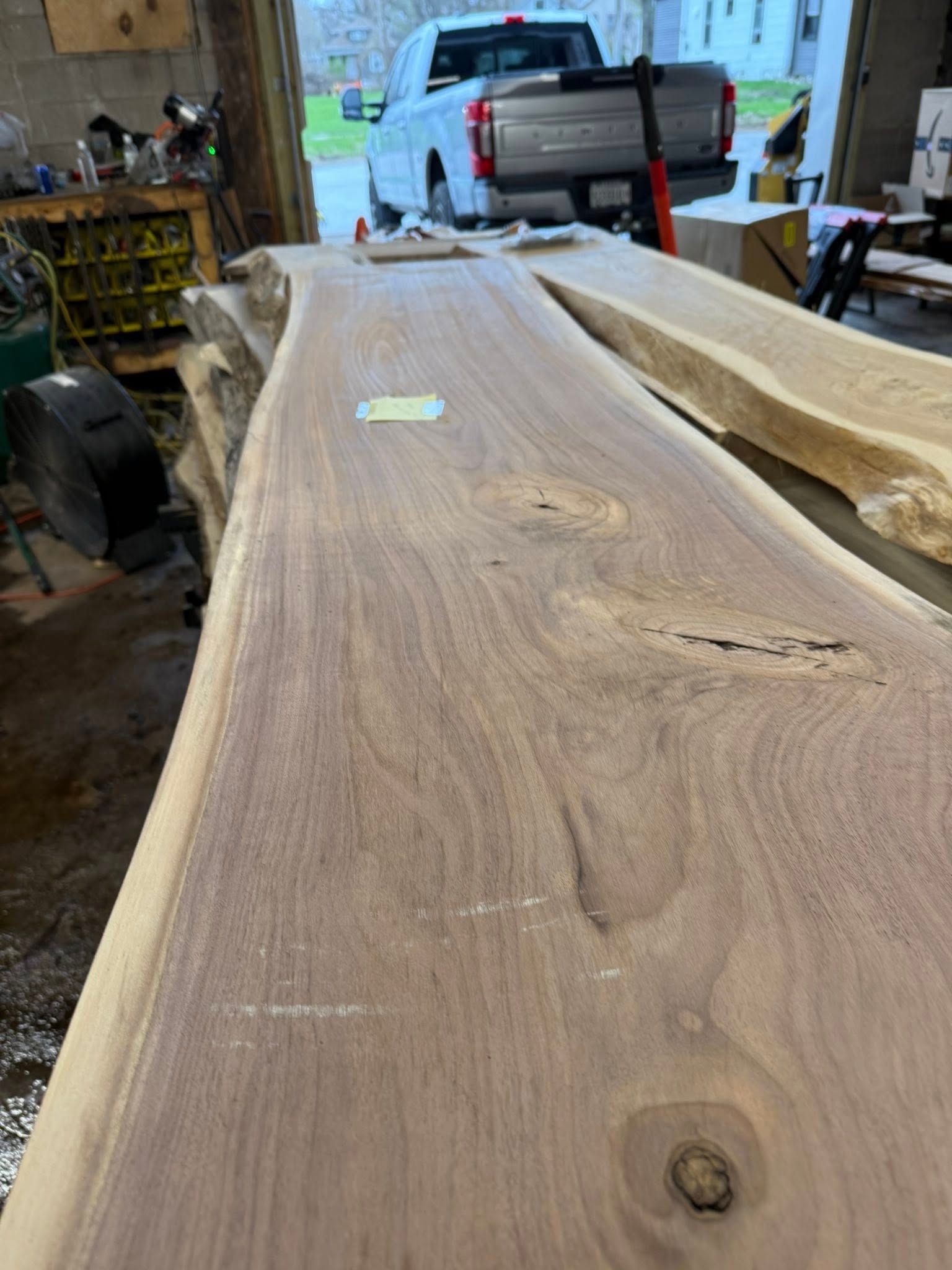 Wood slab on a workbench in a garage, with a truck parked in the background.