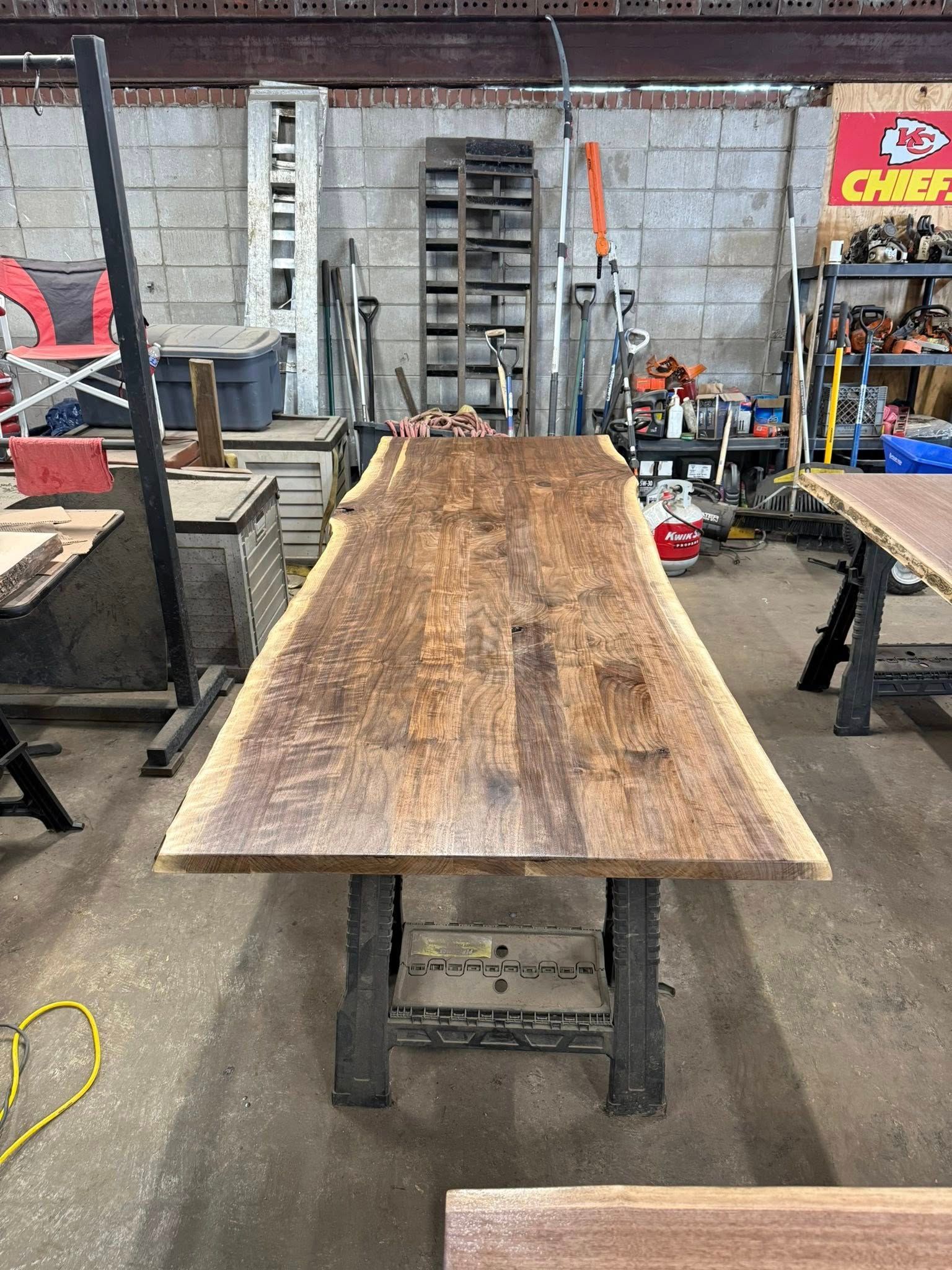 Large wooden tabletop on a metal stand in a workshop, with tools and equipment in the background.