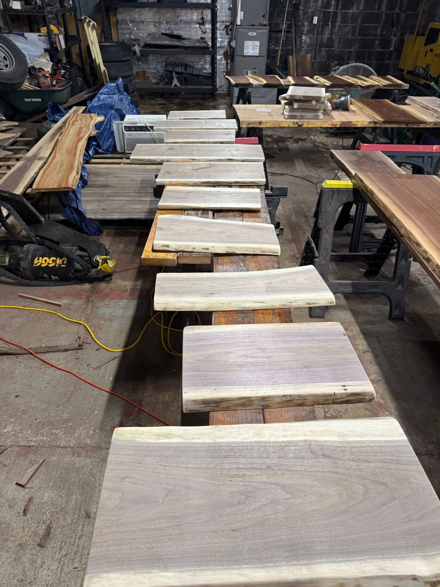 Wooden boards arranged on workbenches in a workshop, with tools and cables on the floor.