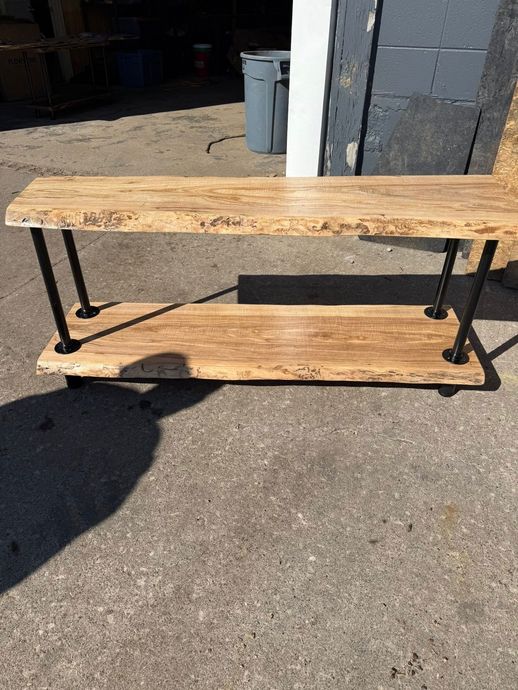 Rustic wooden bench with metal legs sitting on pavement in bright sunlight.