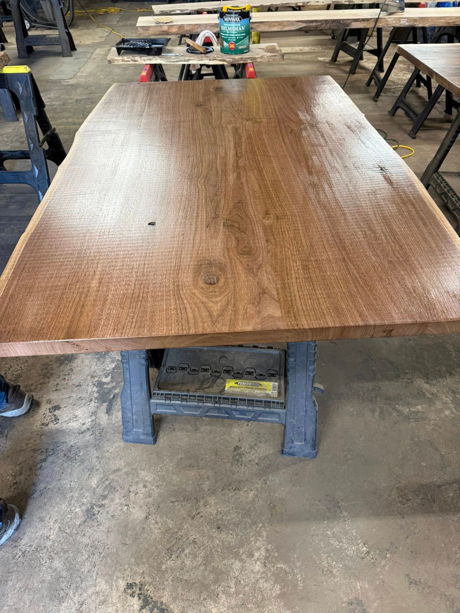 Wooden table in a workshop, with benches and tools in the background.