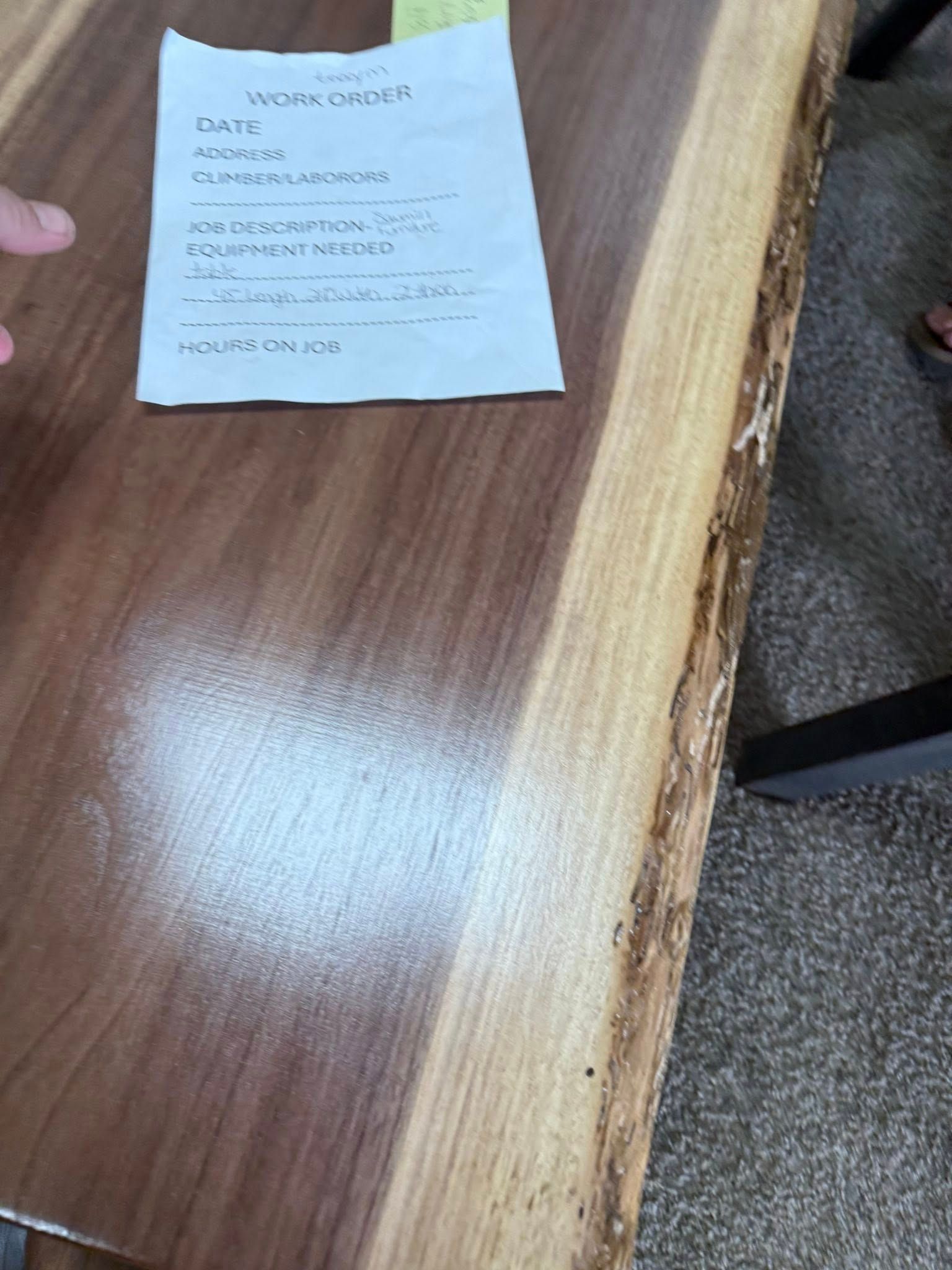 Handwritten note on a wooden desk beside a person’s hand and chair leg
