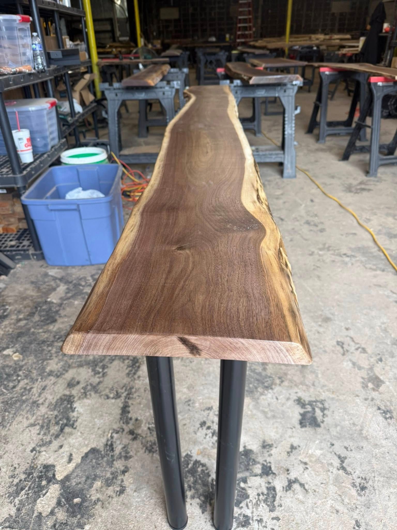 Long live-edge wooden slab on metal sawhorses in a workshop