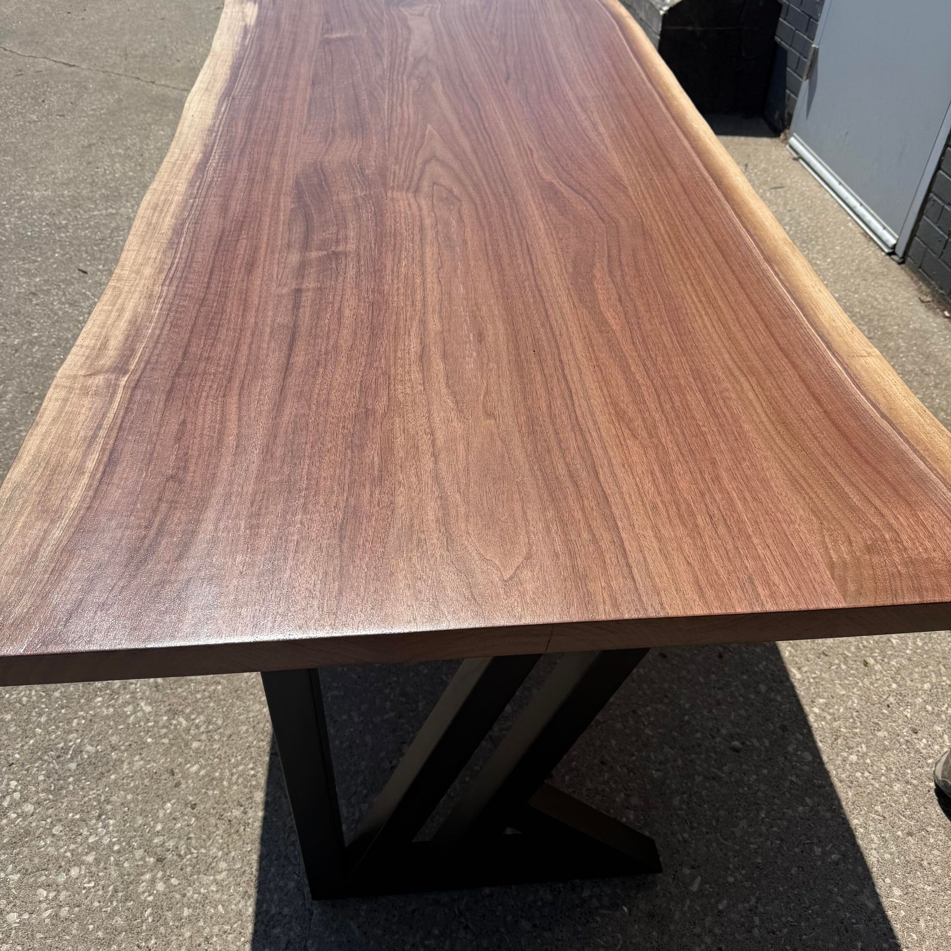 Long wooden tabletop with dark metal legs on a concrete surface outdoors