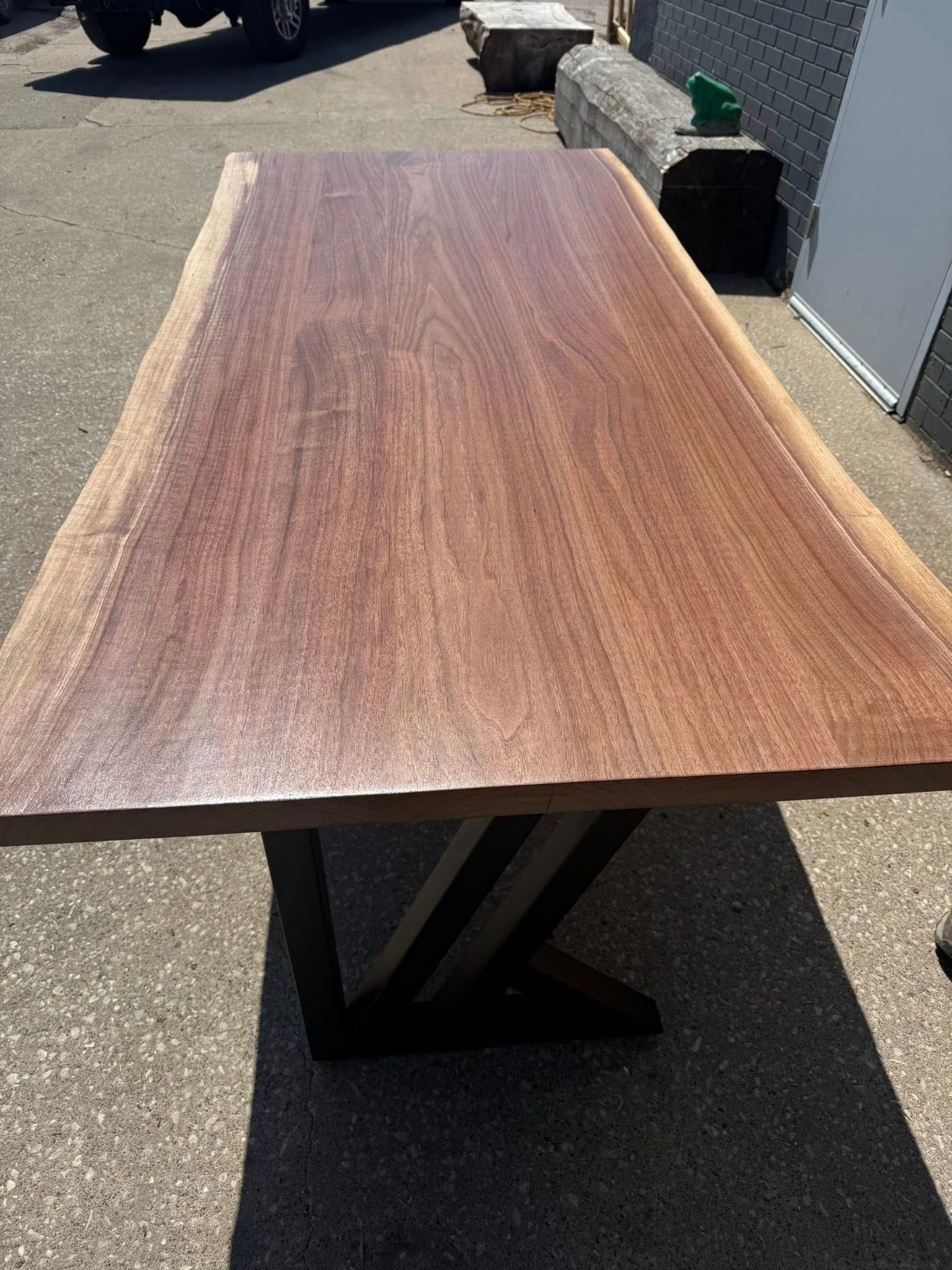 Wooden tabletop with wavy edges on a black metal base outdoors in sunlight.