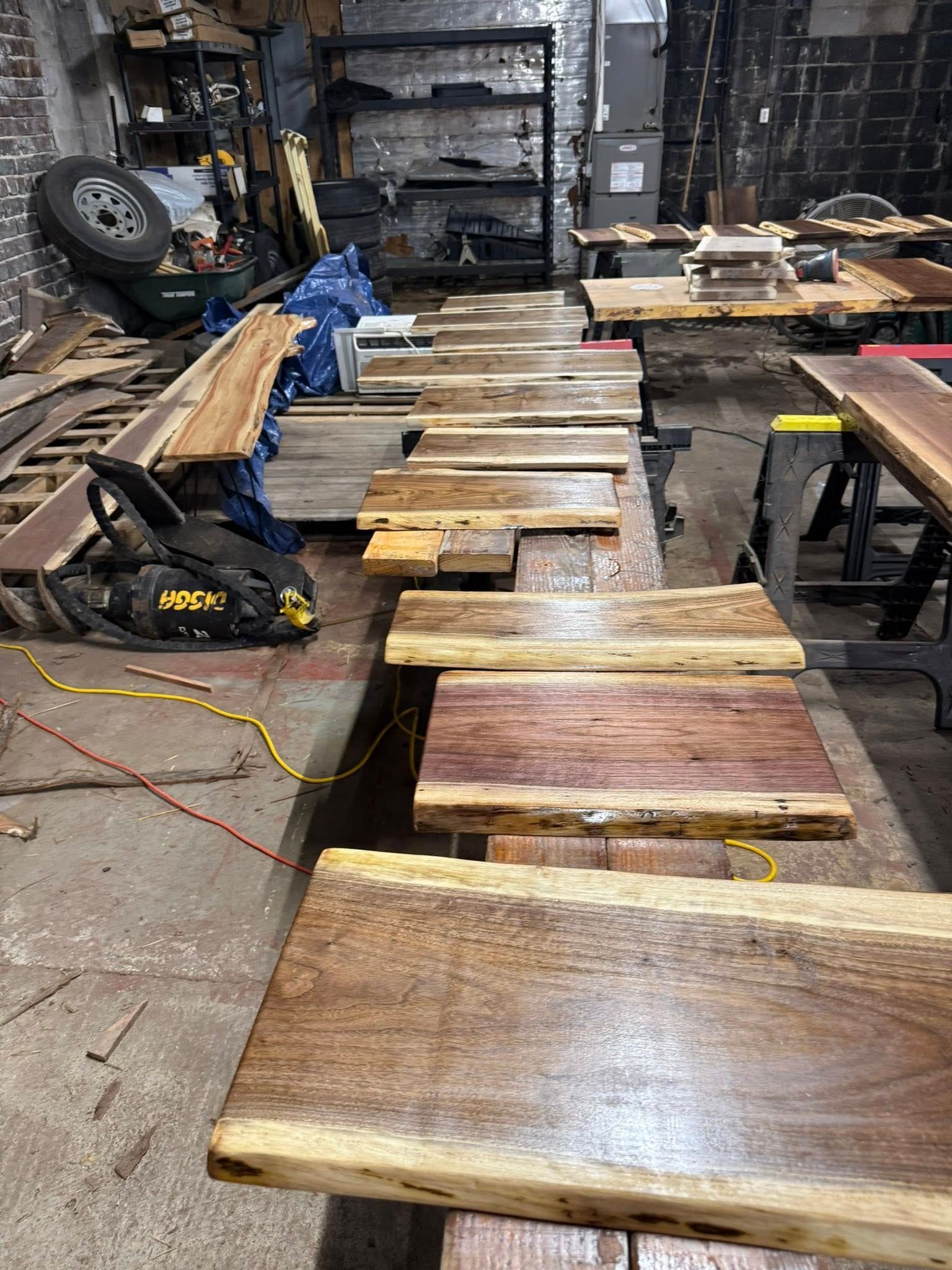 Workshop floor with wooden boards and planks laid out in a row, tools and materials scattered around.