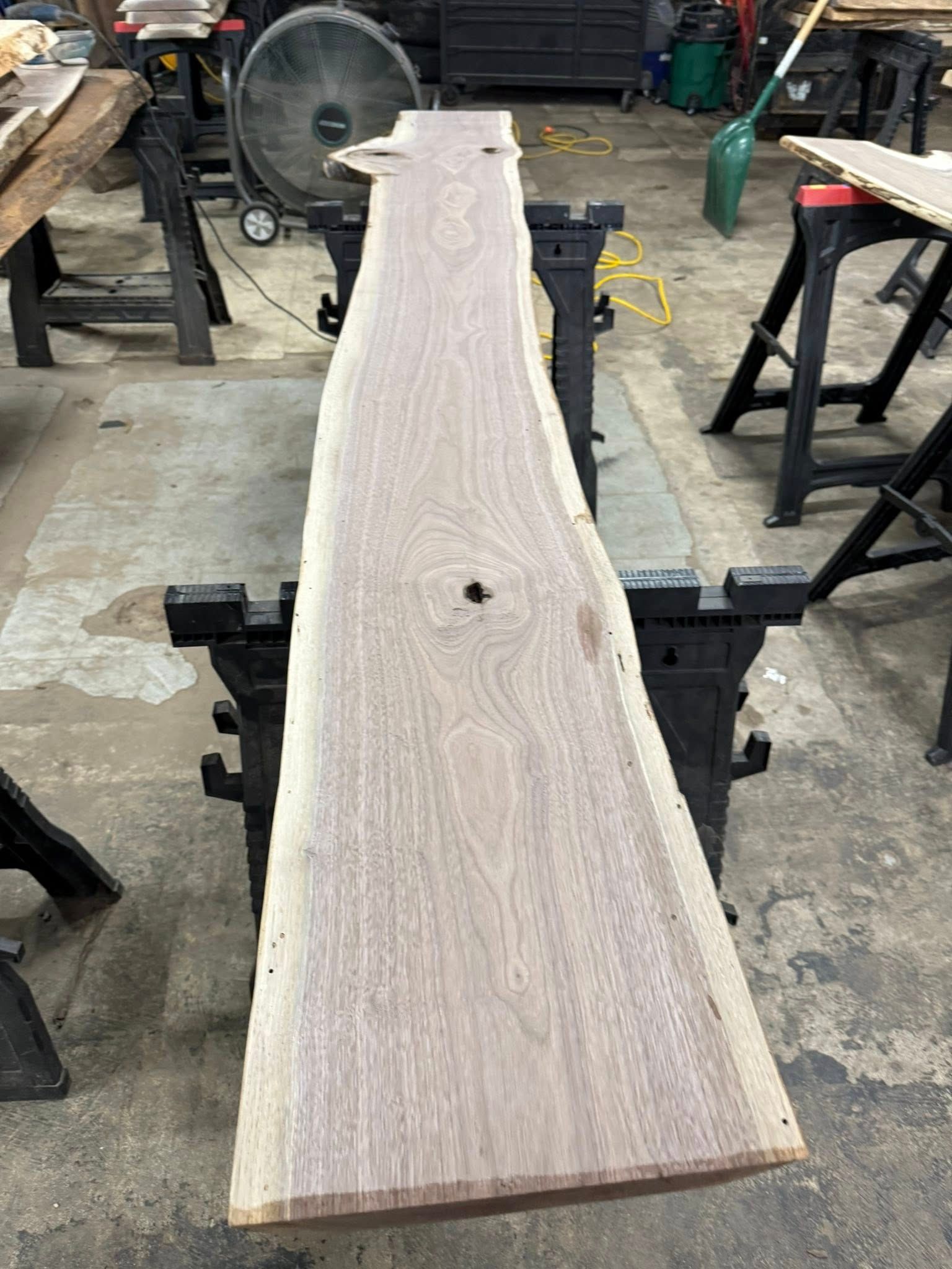Wooden plank clamped in a workshop, showing a pale grain and tapered end.